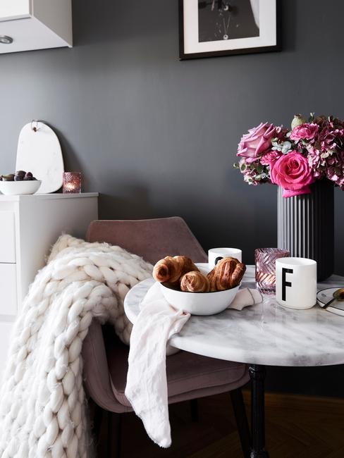 Een zachte witte plaid op fauteuil naast een marmeren bijzettafel met grijze vaas met bloemen