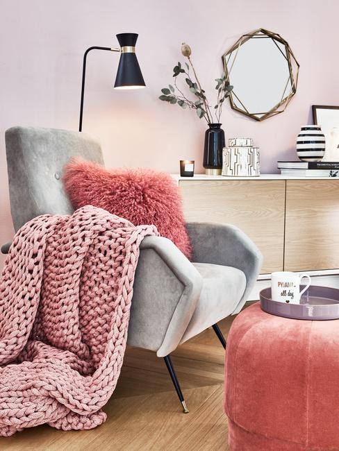 Een grijze fauteuil met sierkussens en zachte chunky knit plaid naast een marmeren bijzettafel met een metalen dienblad