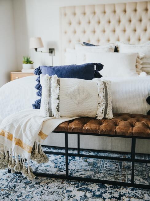 Een slaapkamer met een tapijt in blauwtinten en een bankje met decoratieve witte en blauwe kussens en een deken.