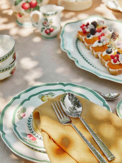 gekleurd servies, zilver bestek en gele servet met gebakjes op tafel
