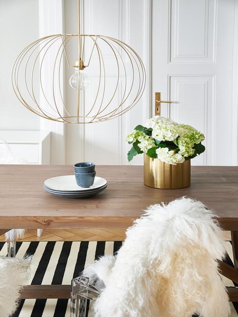 Eettafel met vaas met bloemen en decoratief bord, goudkleurige hanglamp en zwart en wit gestreept vloerkleed