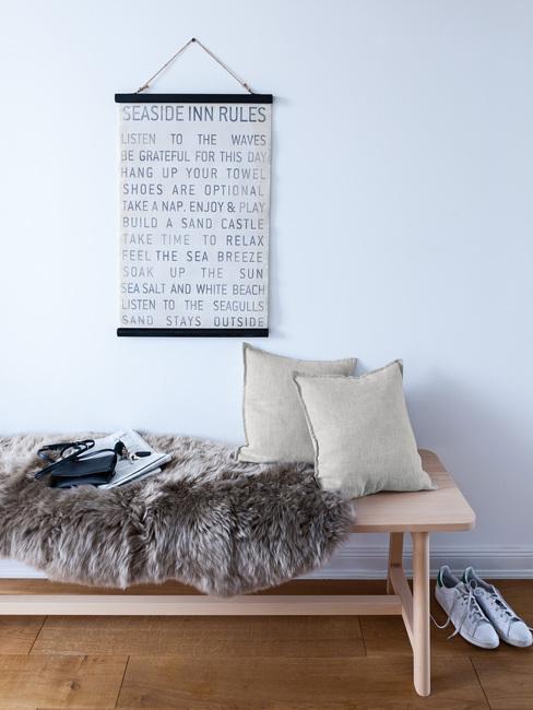 Houten bank met schapenvacht en zachte kussens en print aan de witte muur