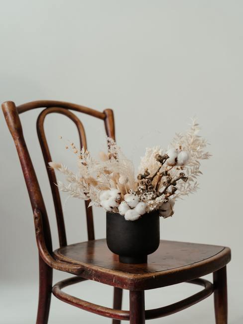 Een boeket gedroogde bloemen in een zwarte lage vaas op een houten stoel in de boho-stijl