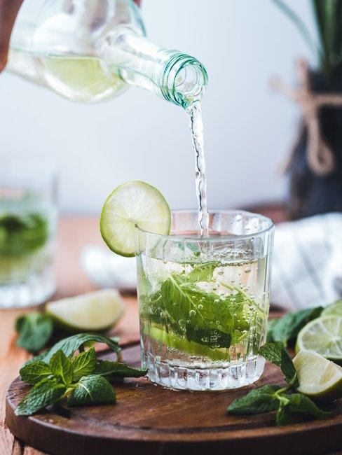 Lifestyle water met limoen Glas met water en groene muntbladeren op houten ondergrond en een glazen fles die water inschenkt