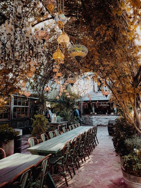 Terras met arabische lampen en groene plantenboog boven lange tafels