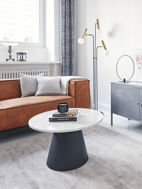 cognac bank, ronde salontafel, wit vloerkleed, grijze kast en lamp in een modern interieur