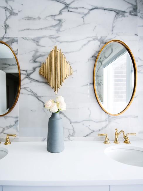 Witte marmere badkamer met een gouden ronde spiegel