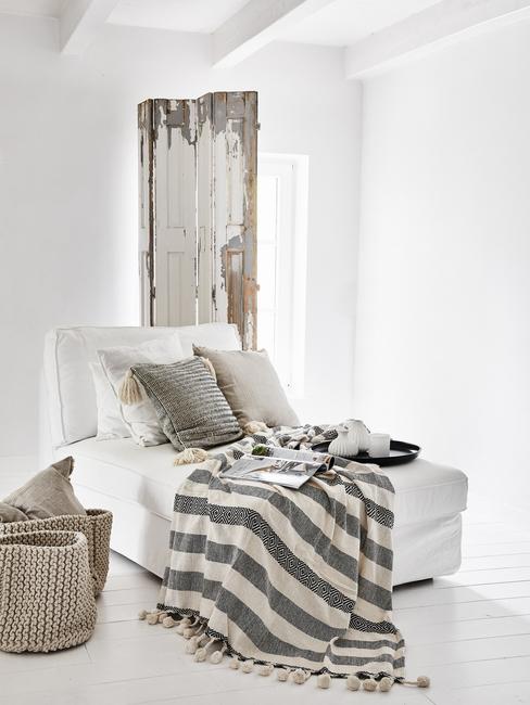Een witte bank met kussens en een plaid in grijs tegen een witte muur in een industriële stijl