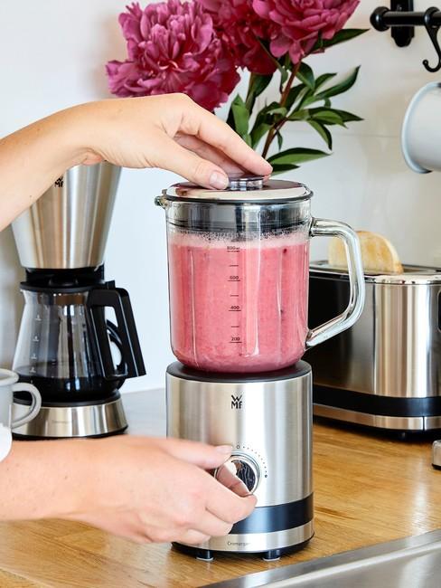 Mixer met detox shake in roze op tafel met toaster en koffiemaker op de achtergrond