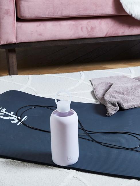 blauwe yogamat met waterfles op een wit kleed en roze bank
