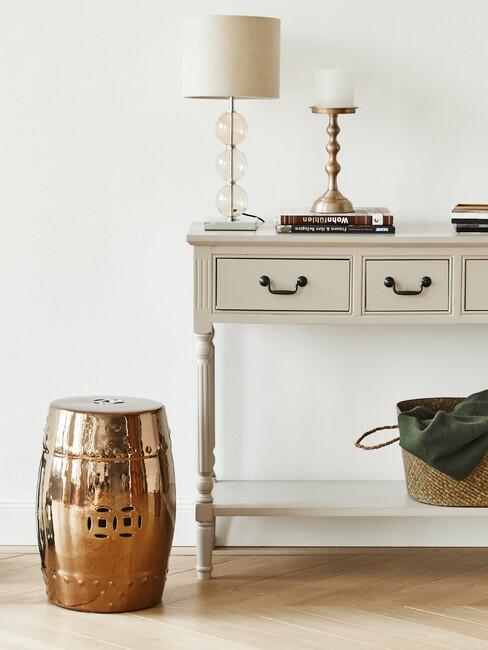 witte landelijke kast met een lamp en kaars er op en naast een kruk in brons kleur