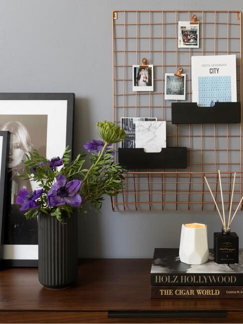 brons kleur rek met fotos boven een dressoir met boeken, bloemen en een poster