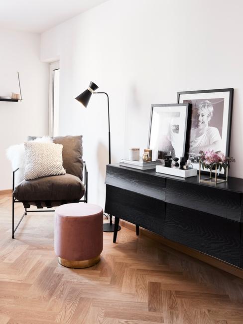Zwarte sideboard van donker hout met ingeliste print en decoraties naas een fluwelen poef en fauteuil