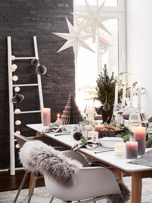 Kerst ontbijt ideeën: gedekte tafel met zilverkleurige serviesset en kaarsen op tafel, stoelen met schapenvacht en verschillende kerstdecoraties