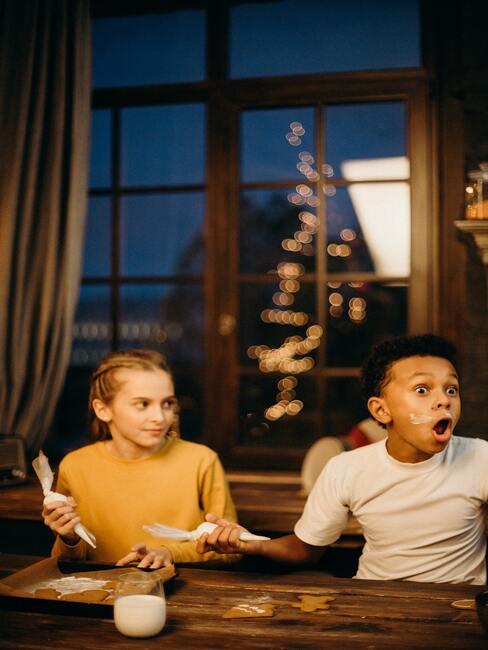Kinderen versieren koekjes aan een grote houten tafel