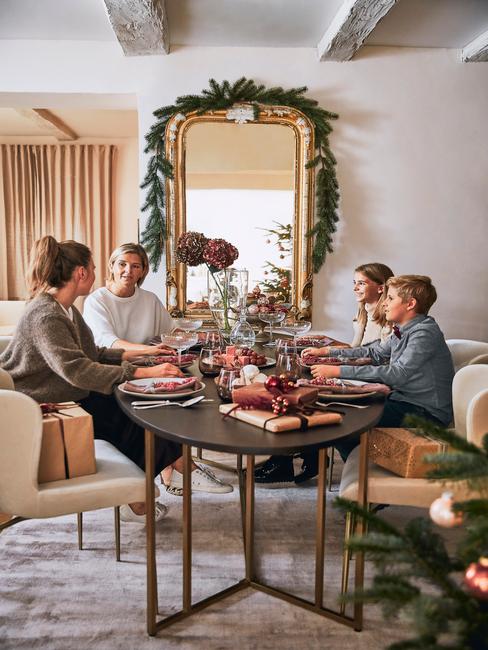 Familie zit aan een grote tafel achter een enorme spiegel met krans