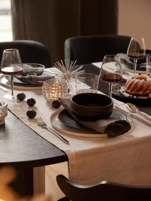 Gedekte tafel met serviesset in zwart, witte tafelloper en kerstdecoratie