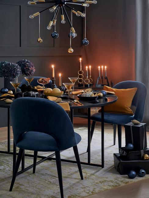 Blauwe stoelen en zwarte, gedekte tafel met serviesset en besteksset in goud kleur en gele servetten