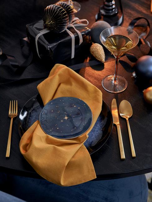 Gedekte tafel met serviesset en besteksset in goud kleur en gele servetten
