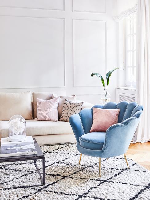 Woonkamer in wit met zitbank in creme en sierkussens naast een fluwelen fauteuil in lichtblauw