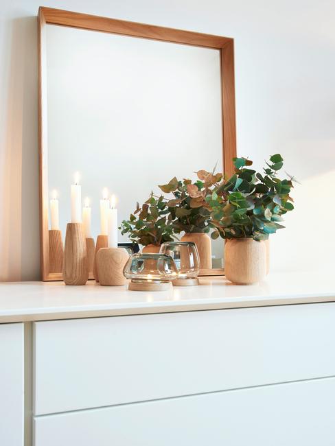 Houten decoratie op een wit dressoir met plantenpot naast een spiegel