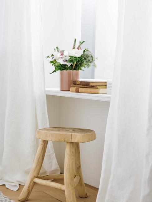 Vensterbank met witte gordijnen naast een houten kruk