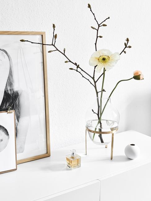Transparant glazen vaas met takken en ingelijste print