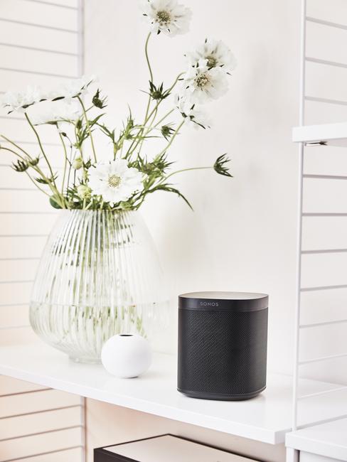 Transparante glazen vaas met bloemen naast zwarte opbergdoos