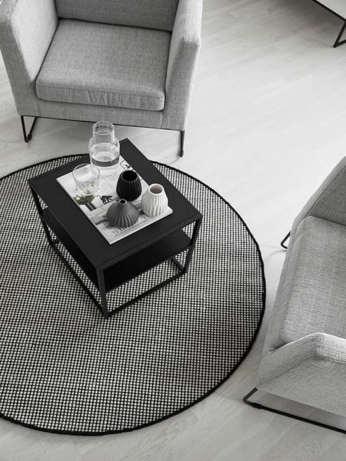 Grijs rond vloerkleed in woonkamer grijze armleunstoelen en zwarte bijzettafel