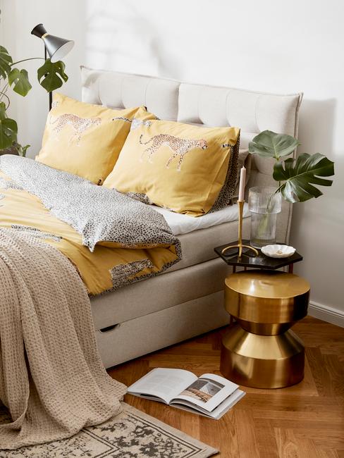 grijze boxspring met gouden tafel en geel dekbed