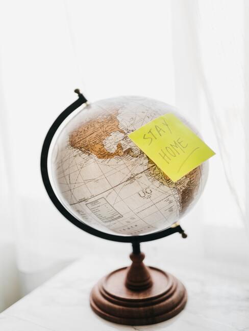 Staycation 1 wereldbl op witte tafel met gele sticker "stay home" - Staycation