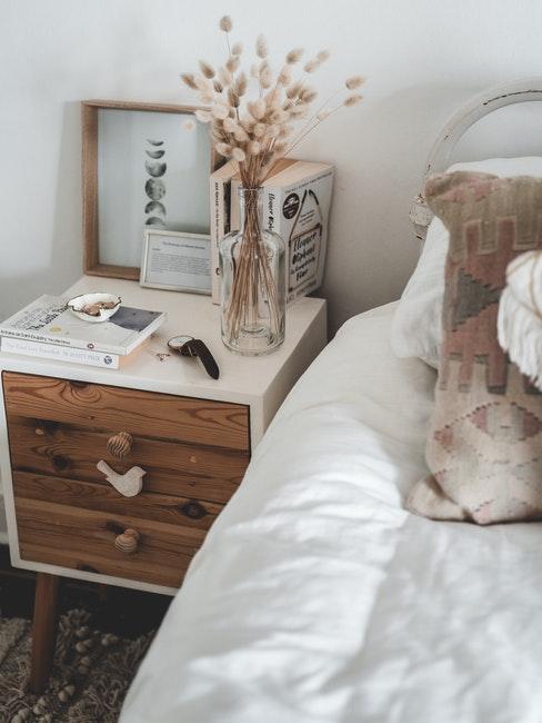 houten nachtkastje met een wit tafelblad naast het bed met wit linnen