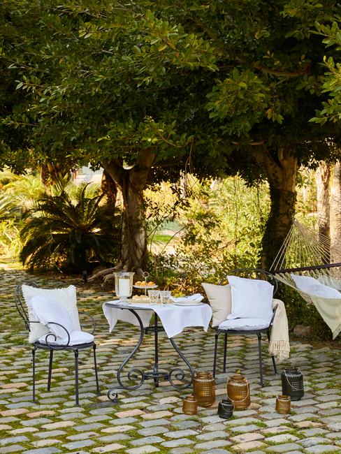 stalen tafel met stoelen en witte kussens in een natuurlijke tuin