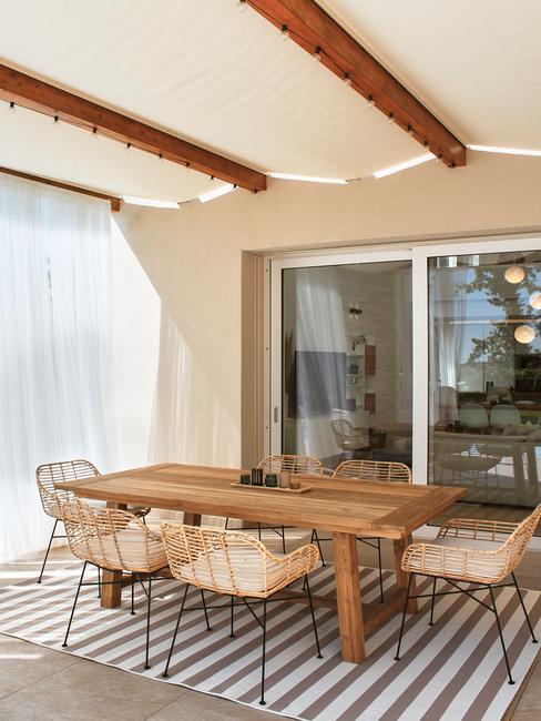 veranda met een houten tafel met rieten stoelen en outdoor kleed