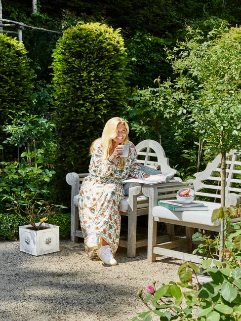 vrouw op een witte houten stoel in een landelijke tuin