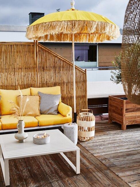 terras met houten planken en gele parasol en witte bank