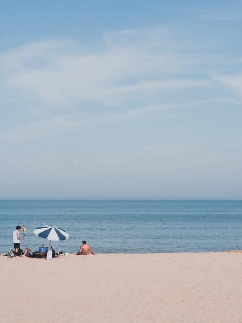 mensen op het strand met een blauw/witte parasol
