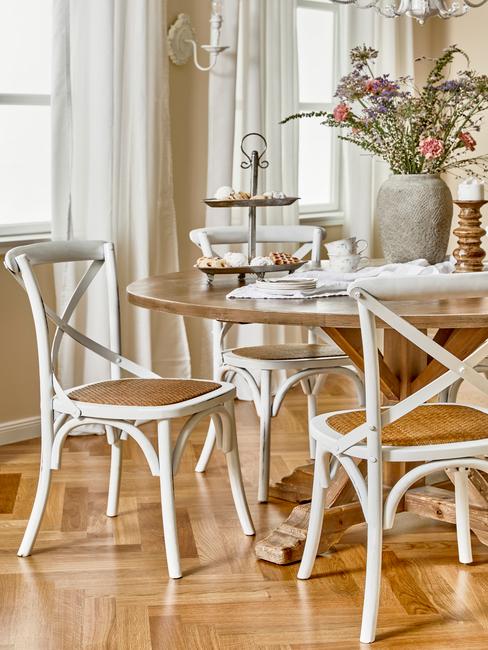 houten tafel met witte stoelen en een grijze vaas met veldbloemen