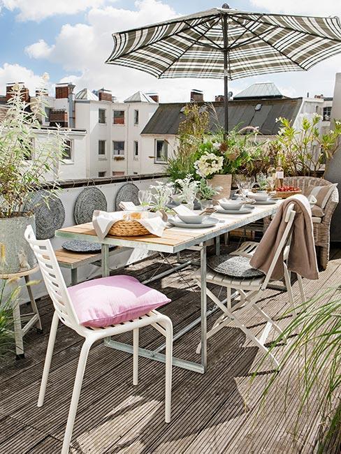 witte tafel en stoelen met gestreepte parasol en roze kussens