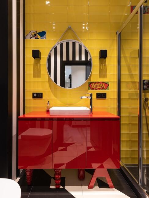 gele muur met rode meubels en ronde spiegel