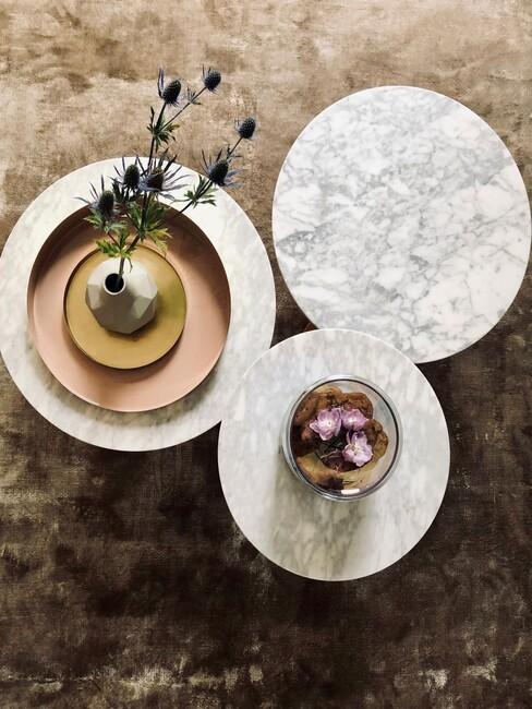 3 marmeren tafels met een gouden vaas met bloemen op een groen warm kleed