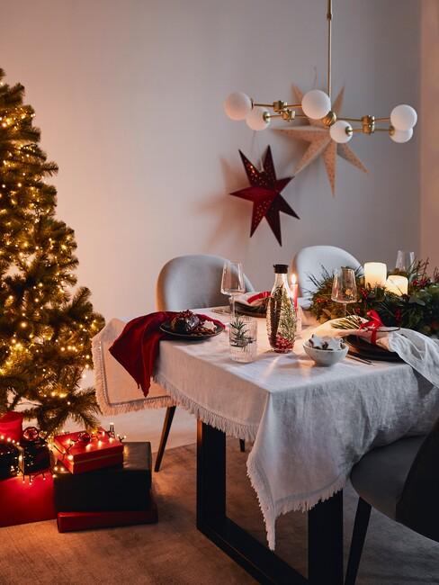 tafel met wit tafelkleed grijze stoelen en gouden hanglamp met een kerstboom