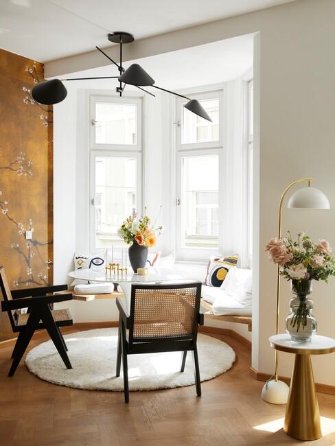 okergeel behang met een ronde eettafel en houten stoelen