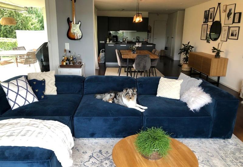 Grote open woonkamer met blauwe bank en ronde houten salontafel
