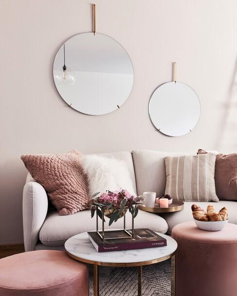spiegelwand met ronde spiegels boven een beige bank en rode kussens