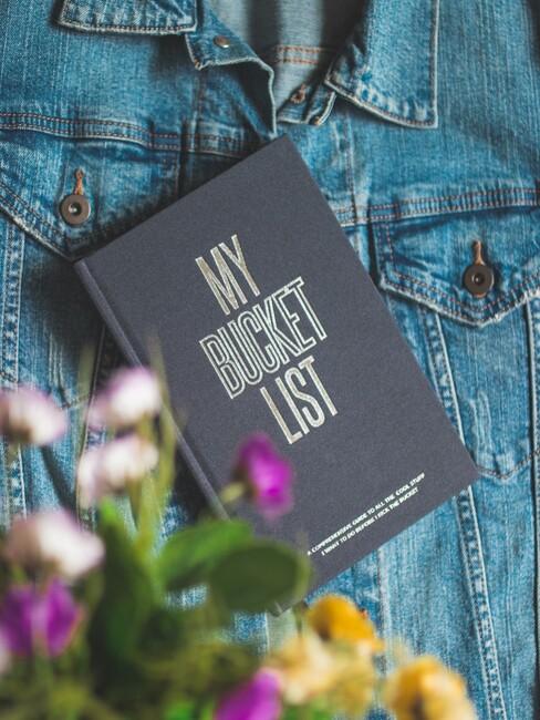 Zwart boekje met bucketlist erop en een spijkerjas