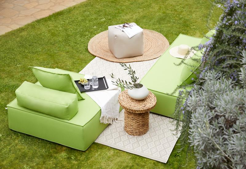 scandinavische tuin met een jute vloerkleed, rotan bijzettafel en loungebanken