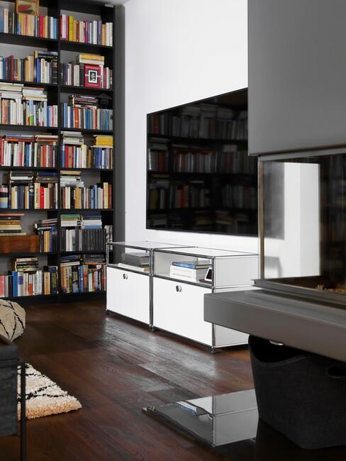 grote tv aan witte muur naast een boekenkast