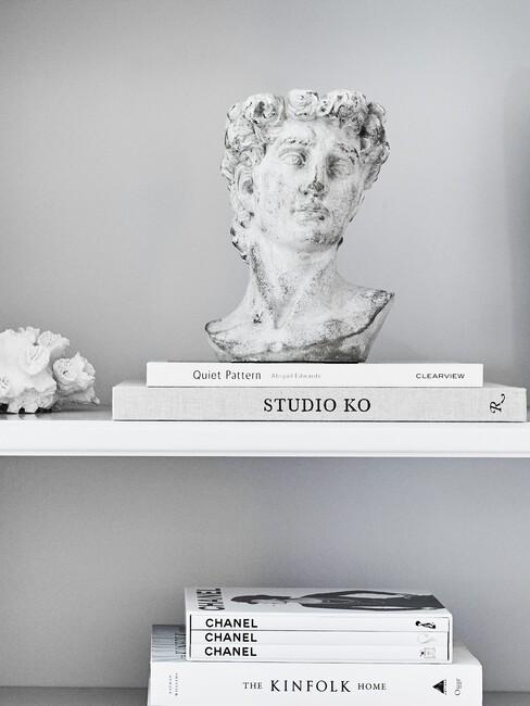 decoratieve boeken en witte beelden in een witte boekenkast