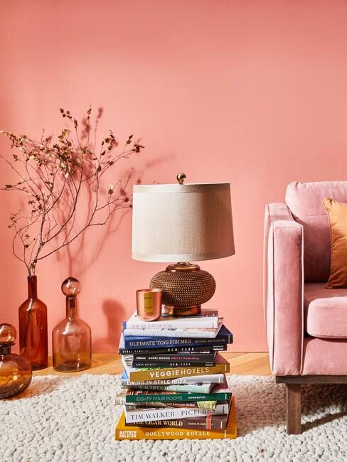 decoratieve boeken als bijzettafel waaop een lamp staat naast een roze bank